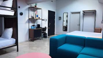 Una habitación de hotel moderna con una cama litera, un escritorio con silla, una mesita redonda pequeña, un sofá, un armario y un espejo.