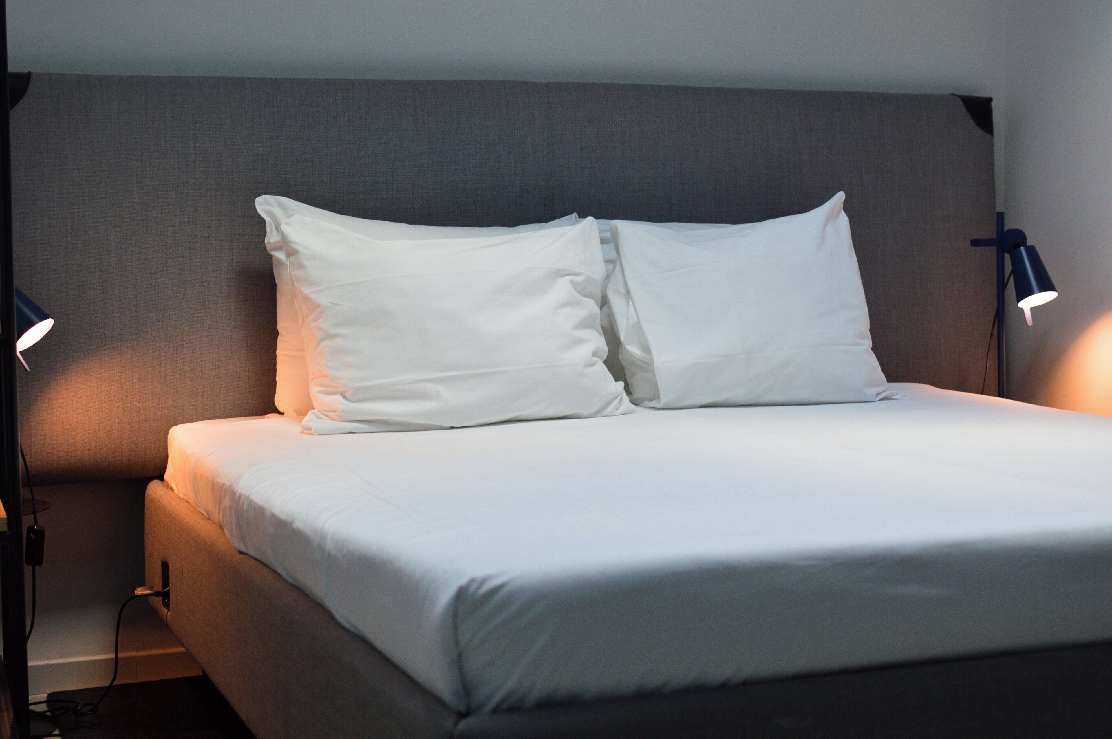 A neatly made bed with white linens, two bedside lamps, and a headboard.