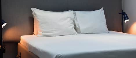 A neatly made bed with white linens, two bedside lamps, and a headboard.