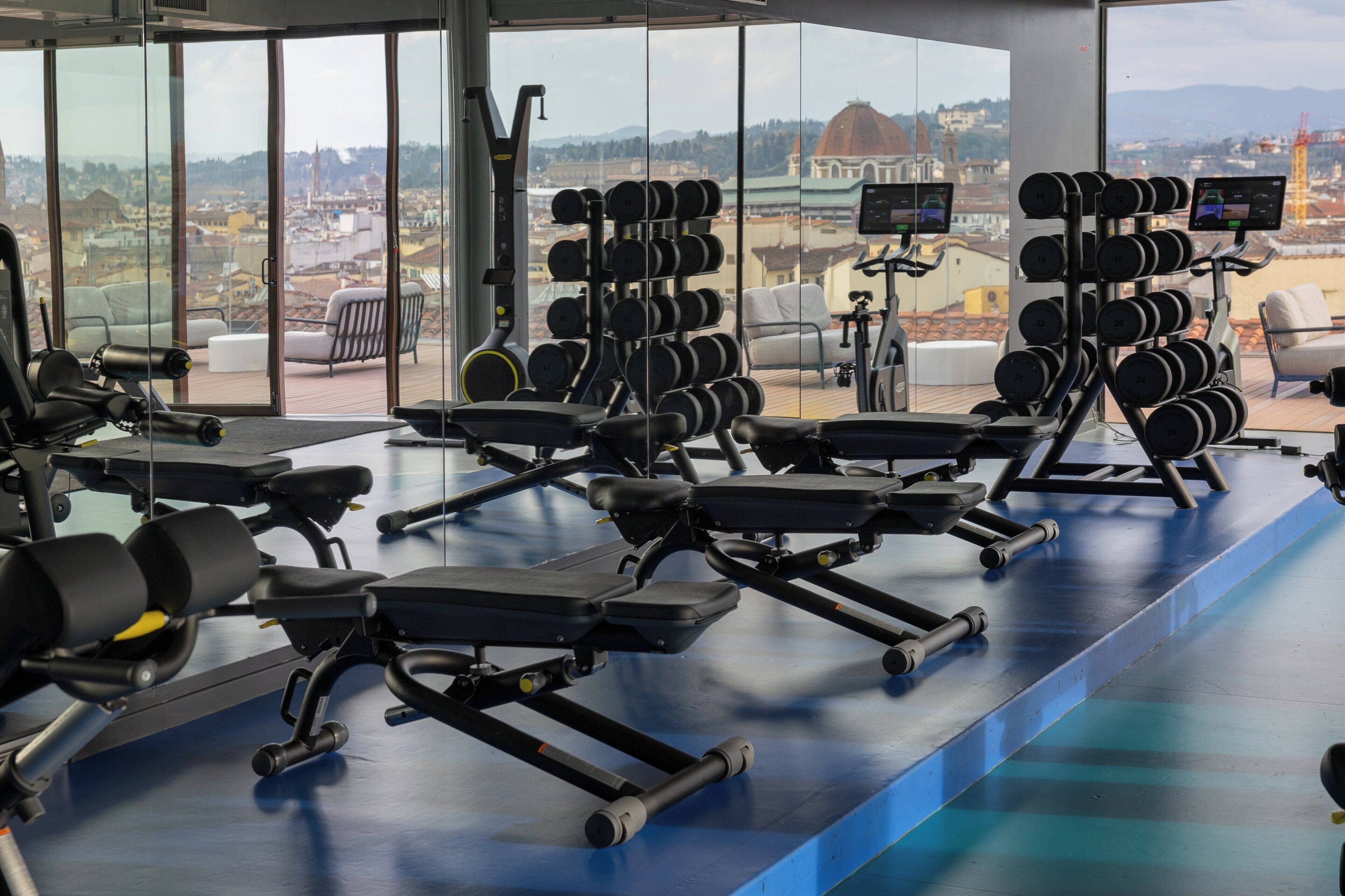 Un gimnasio con equipamiento de ejercicio y vistas a un paisaje urbano.