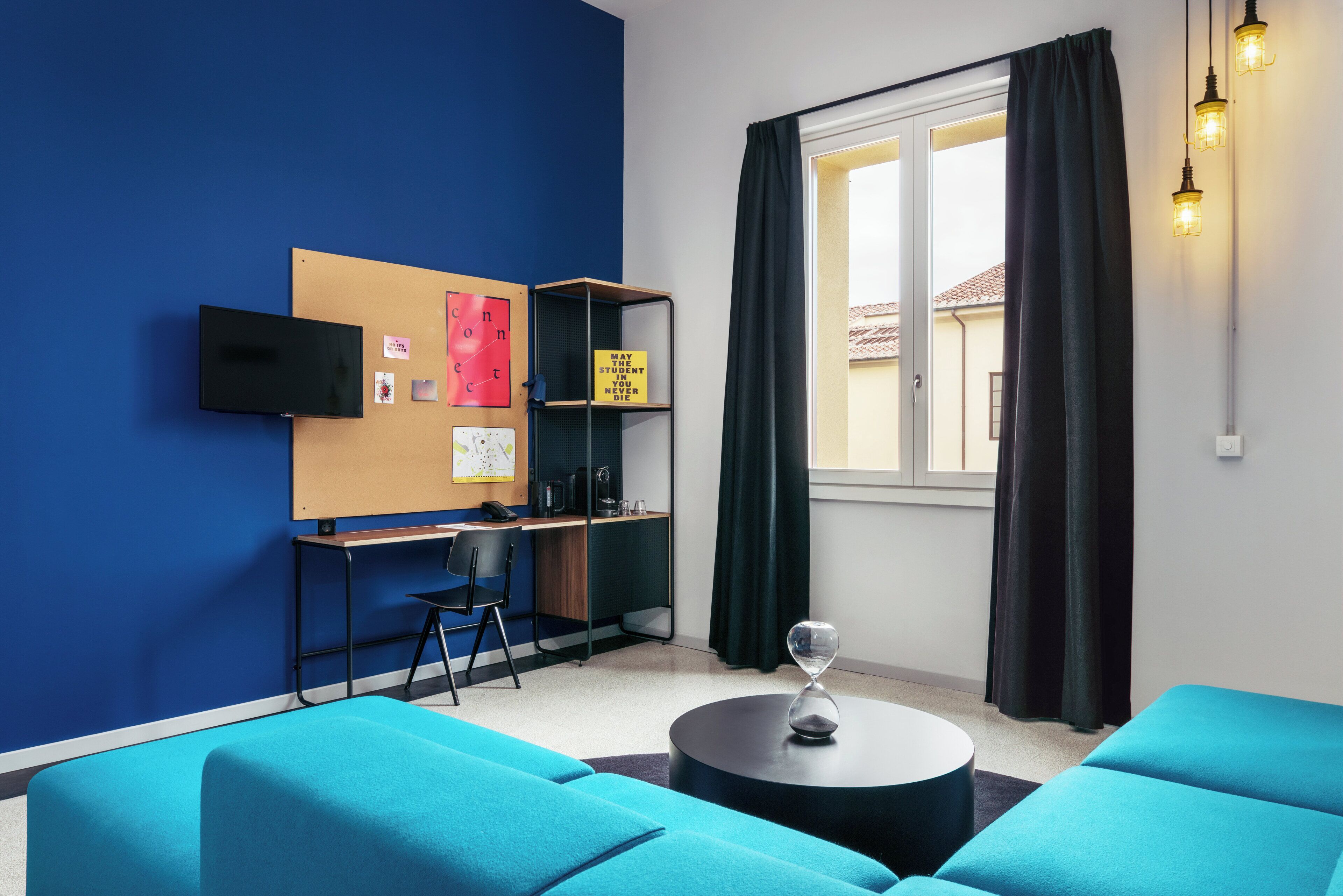 Une pièce moderne aux murs bleus, avec un bureau et une chaise, une table ronde et une grande fenêtre avec des rideaux.