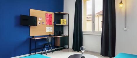 Une pièce moderne aux murs bleus, avec un bureau et une chaise, une table ronde et une grande fenêtre avec des rideaux.