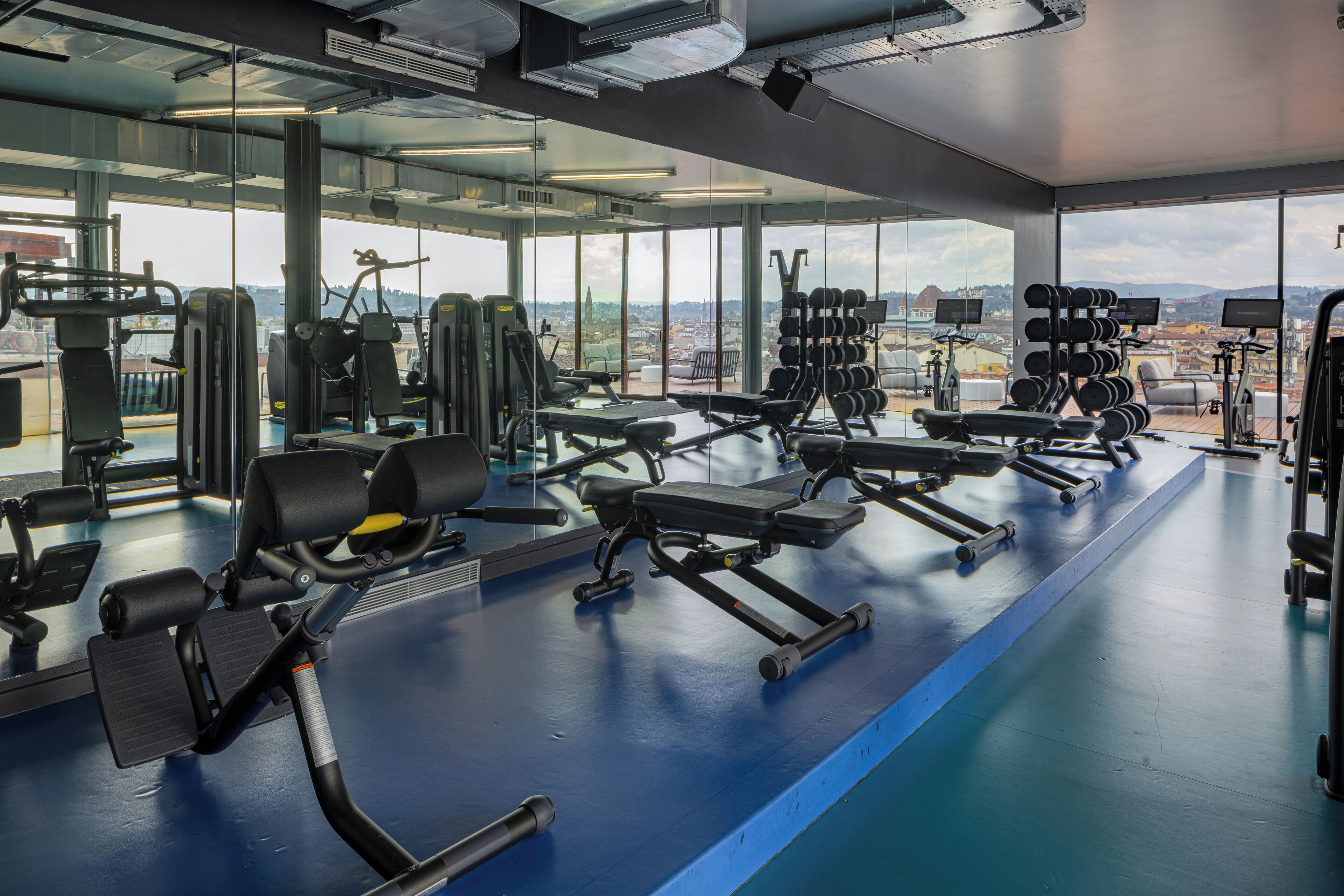 A gym with various exercise equipment, large windows, and a view of the city.