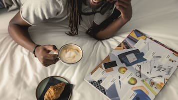 Una persona sdraiata su un letto con un libro, una tazza di caffè e un dolce.