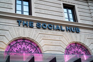 Een gevel met het bord 'THE SOCIAL HUB' boven twee boogvensters met decoratief ijzerwerk.