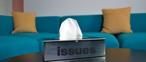 A tissue box labeled "issues" on a table in front of a blue sofa with striped cushions.