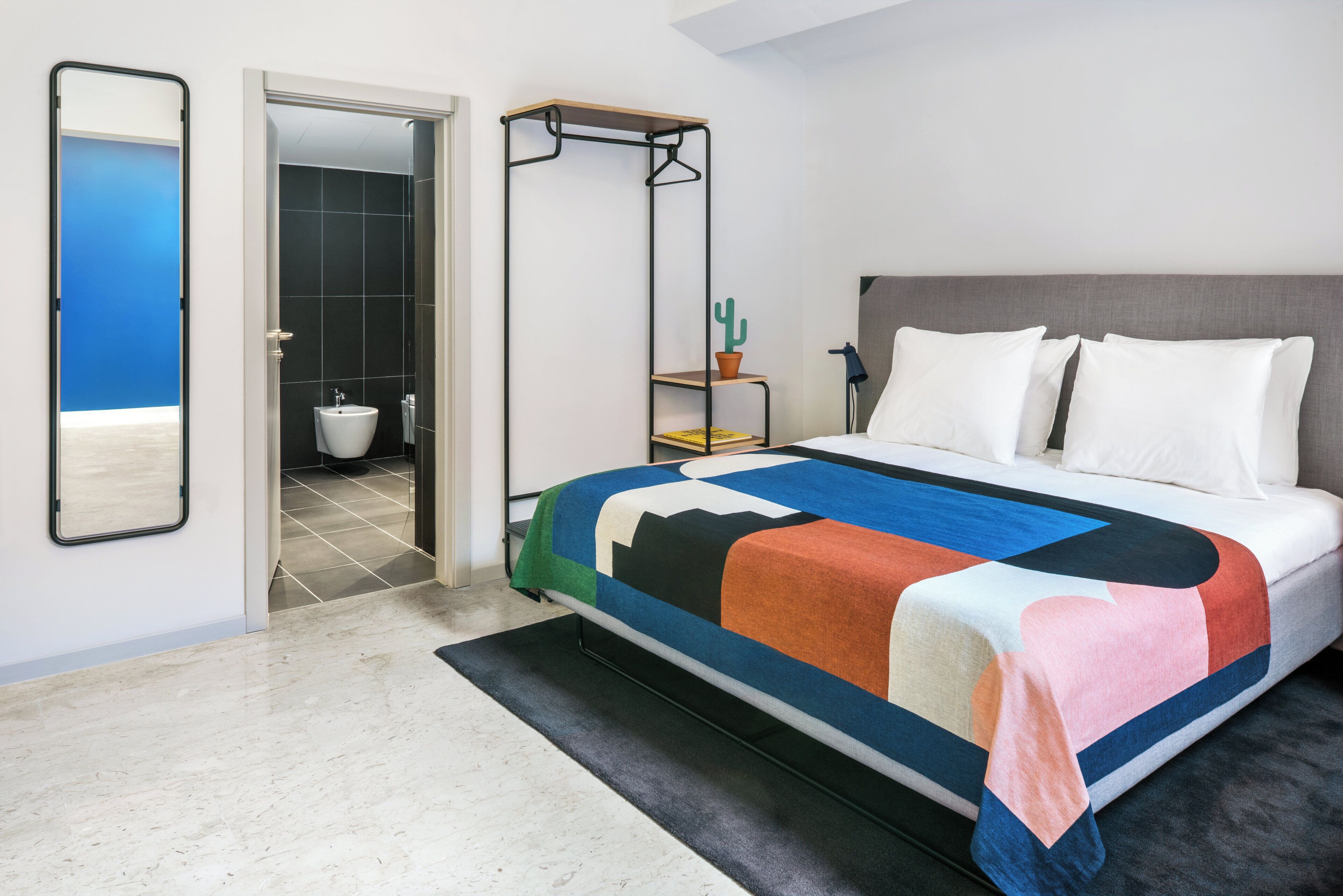 Un dormitorio con cama, mesita de noche, sillón colgante, espejo y baño visible a través de una puerta abierta.