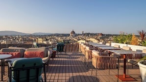 Terraza en la azotea con mobiliario exterior, vista a un paisaje urbano y una cúpula destacada en la lejanía.
