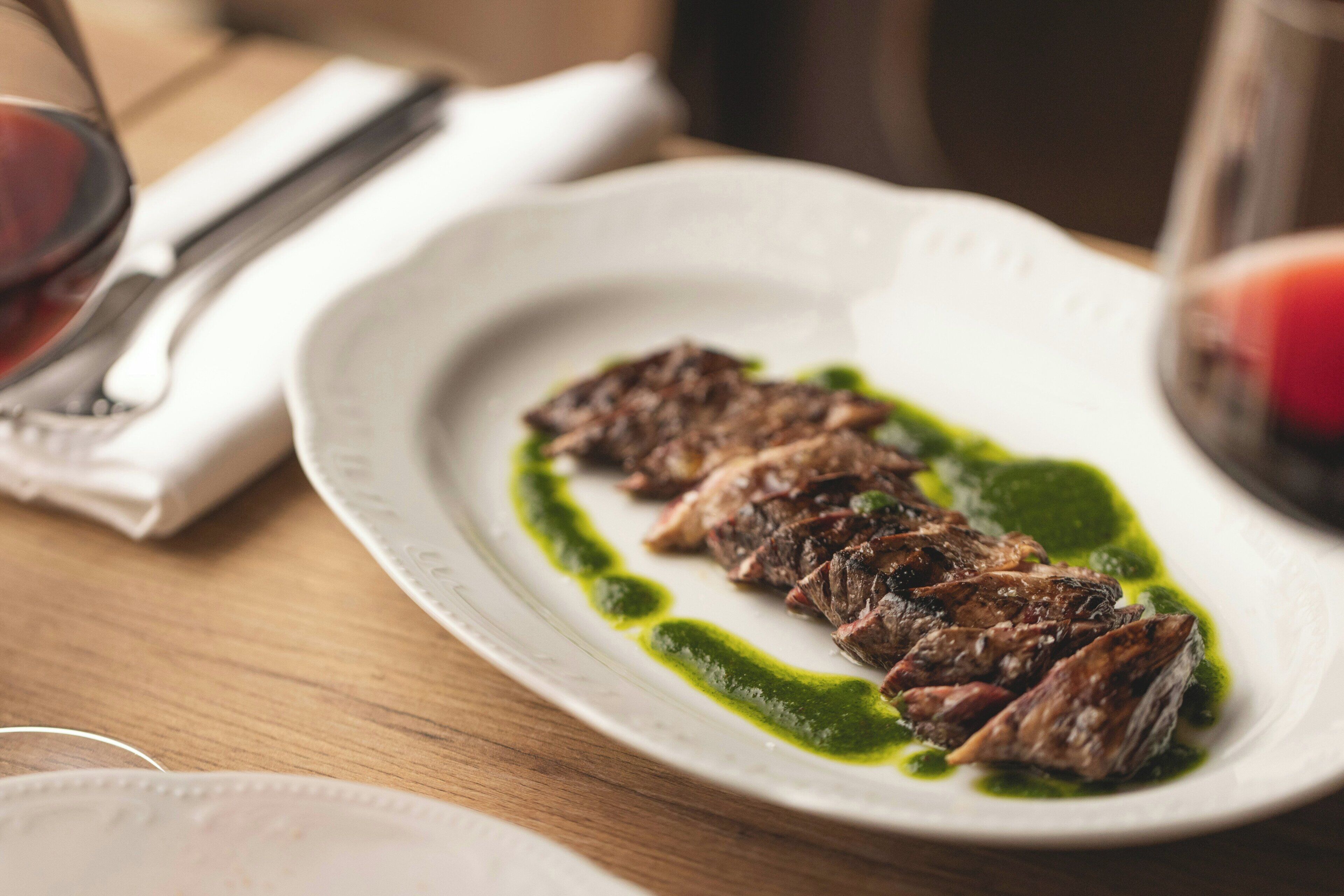 A plate of sliced meat with a green sauce on a white plate.