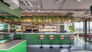 Un área de bar moderna con detalles verdes, distintas opciones de asiento y vistas a la ciudad.