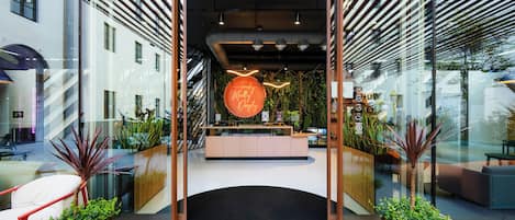 Un área de recepción moderna con un mostrador central, paredes de vidrio y plantas en macetas.