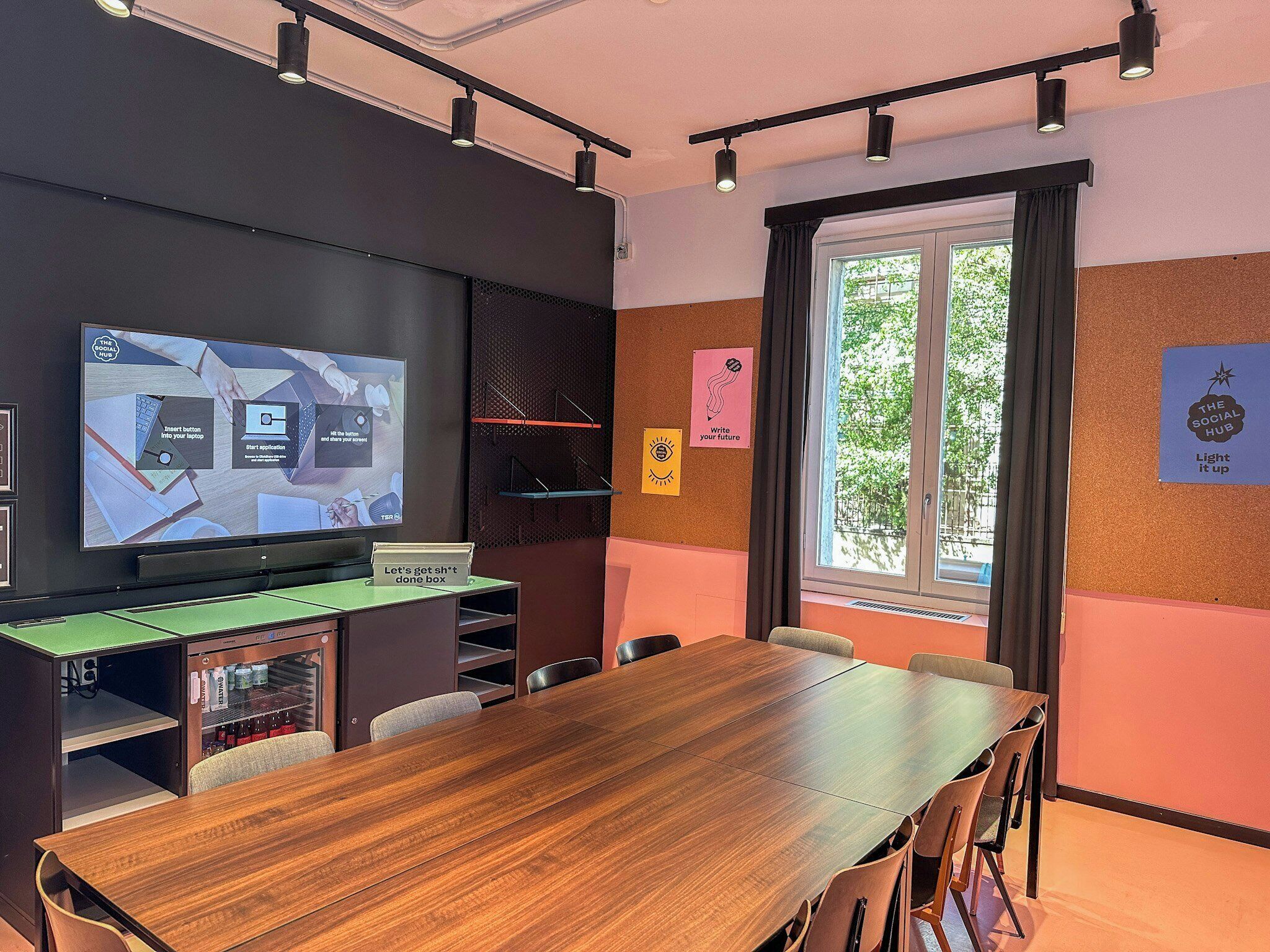 Ein Konferenzraum mit einem Holztisch, Stühlen, einer großen Leinwand und motivierenden Postern an den Wänden.