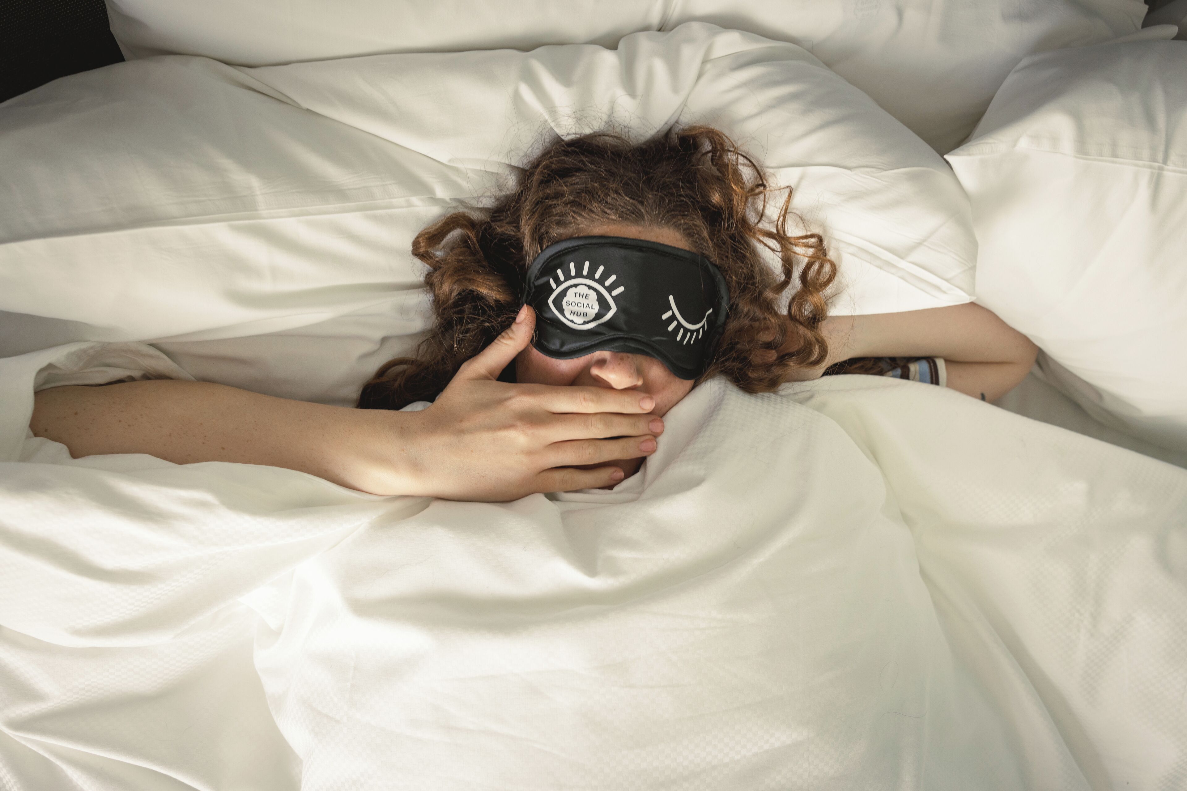 Eine Person liegt auf einem Bett mit einem weißen Kopfkissen und einer Schlafmaske.