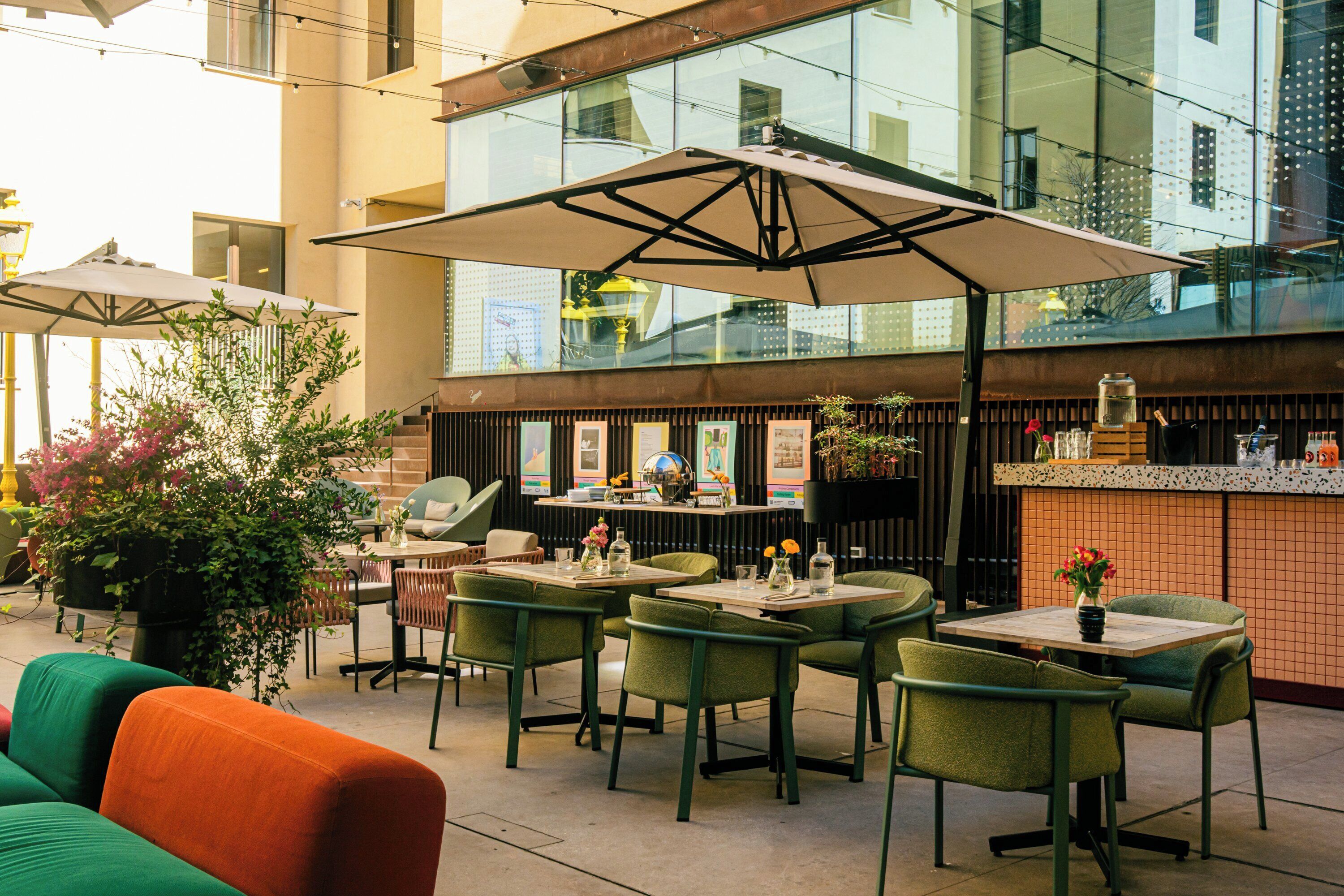 An outdoor dining area with tables and chairs, a large umbrella, and a potted plant.