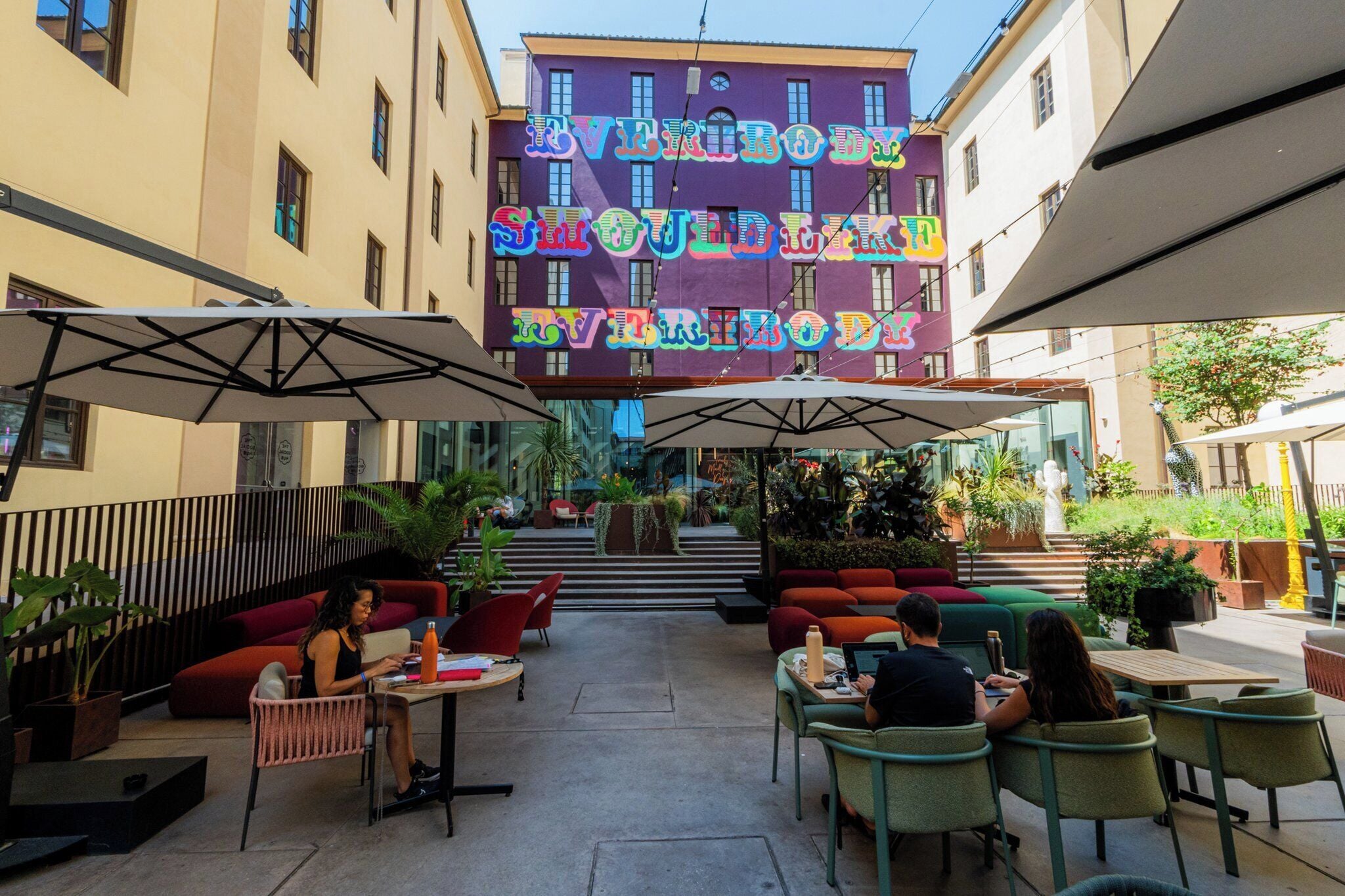 An outdoor seating area with tables and chairs, surrounded by plants and a staircase leading to an upper level.