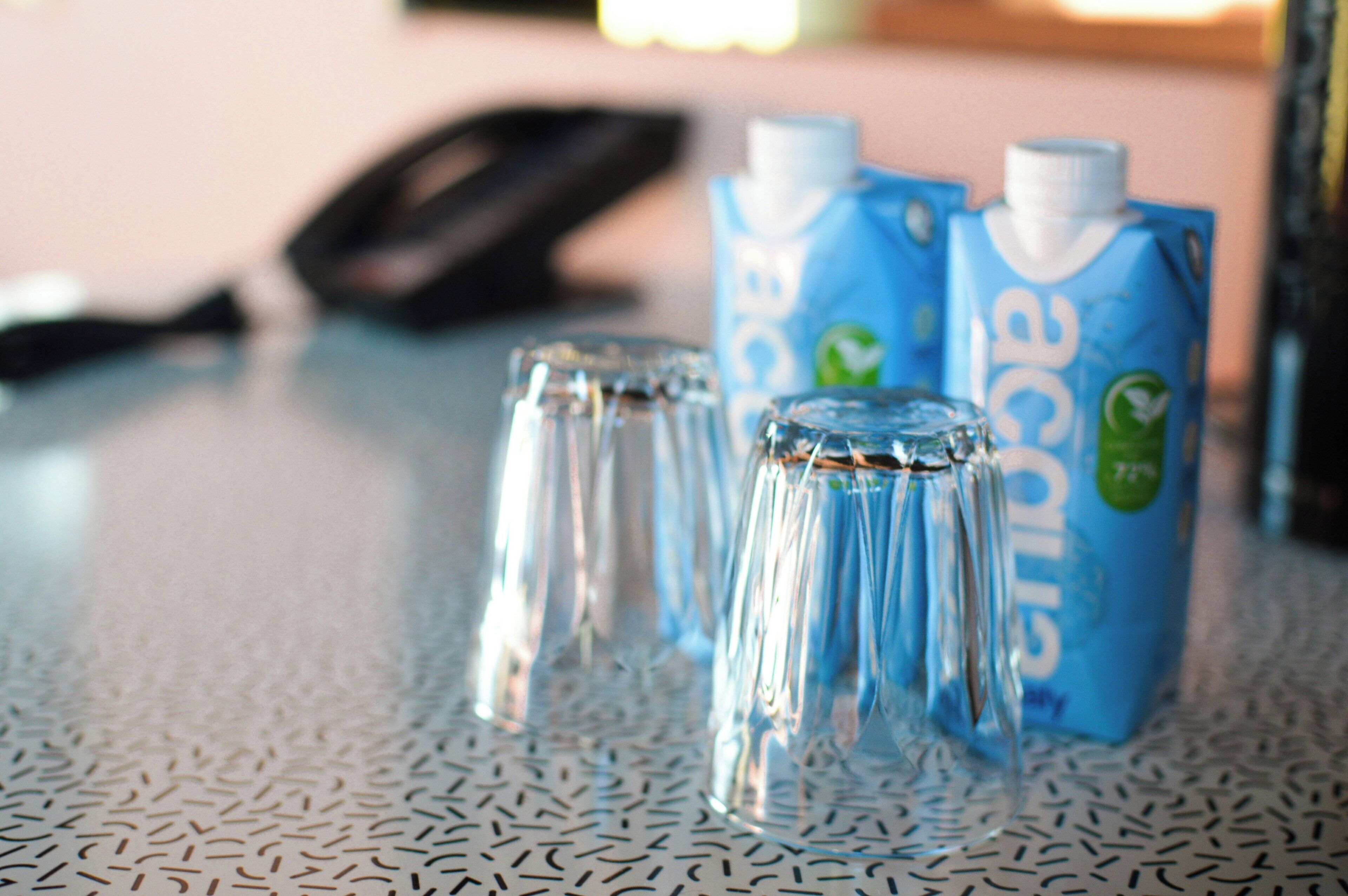 A metal table with three clear glasses and two blue cartons of water.