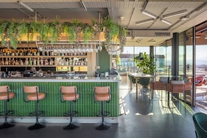 A bar area with a green bar counter, multiple stools, and a variety of bottles and glasses. - The Social Hub Florence Lavagnini (Florence)