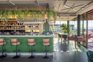 A bar area with a green bar counter, multiple stools, and a variety of bottles and glasses.