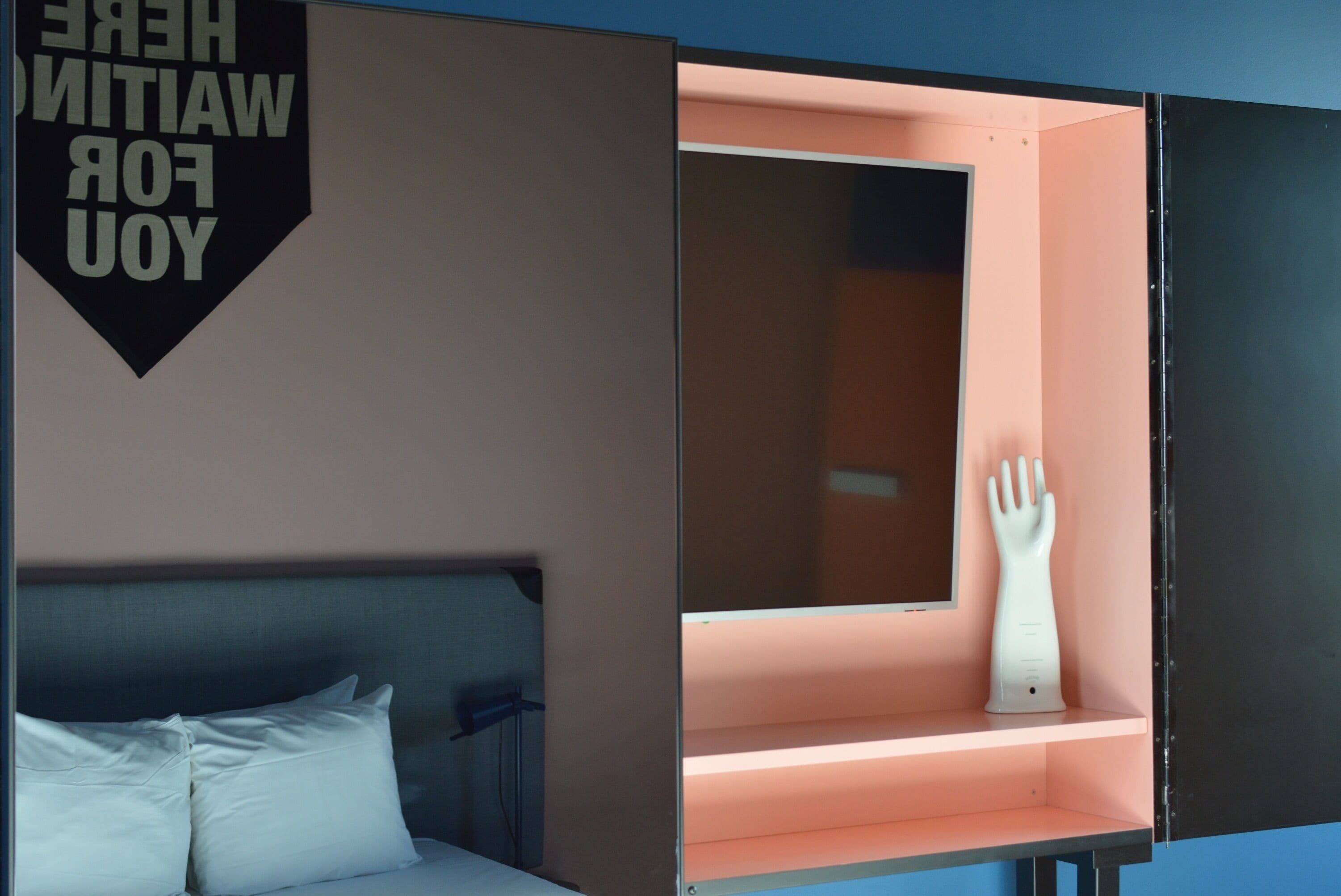 A room with a bed, a wall-mounted sign, and a cabinet with a hand-shaped object inside.