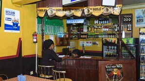 Eine Bar mit Empfangsbereich, Barhocker und einer Theke. Schilder werben für 'Nille Special' und 'Club Shorts'.
