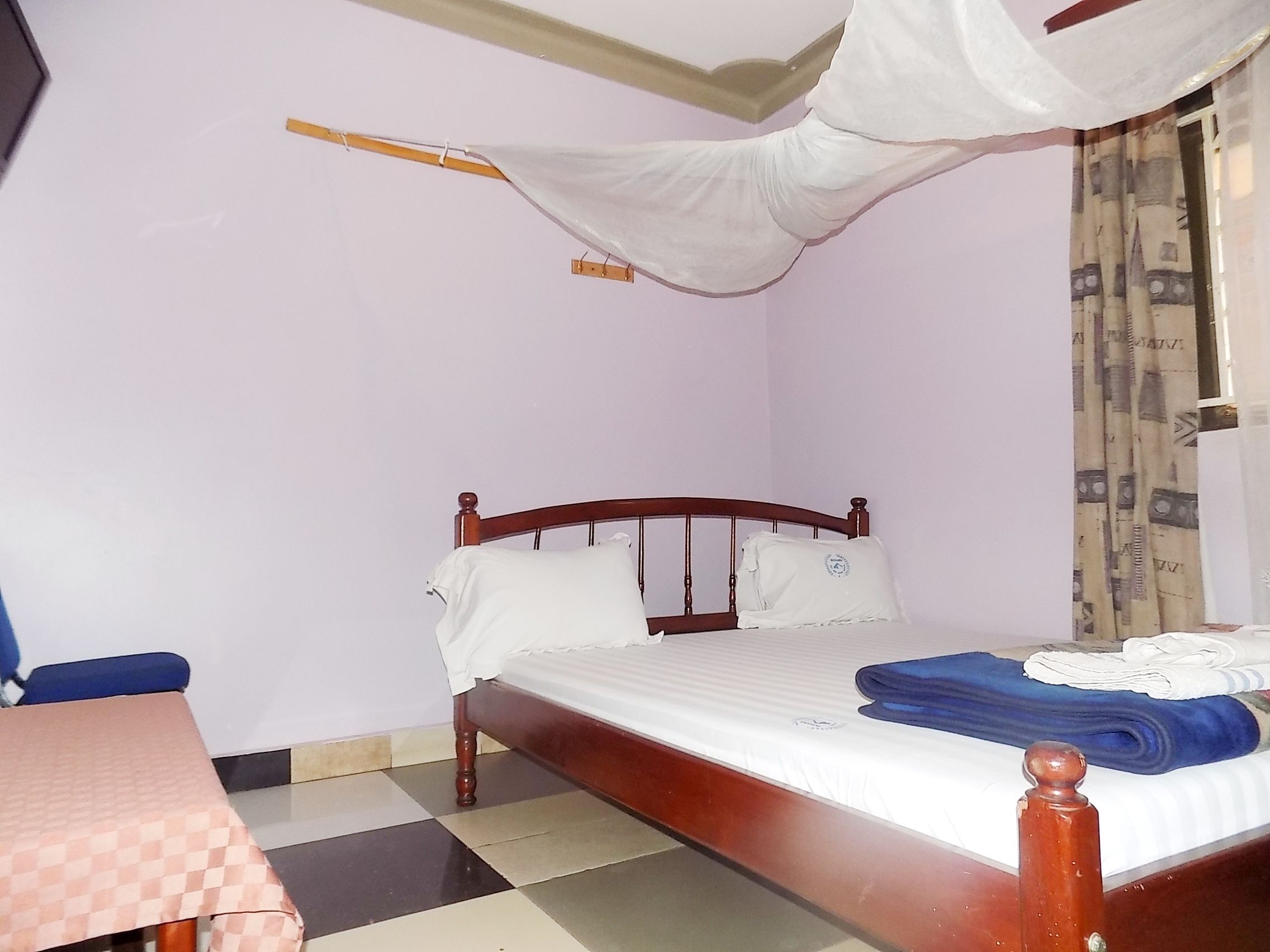 Ein Schlafzimmer mit einem hölzernen Bett, einem Schachbrettfußboden, einem Tisch und einem Moskitonetz.