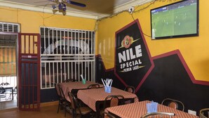 Ein Restaurant mit karierten Tischdecken, Metallstühlen und einem großen Wandgemälde, das Nile Special Premium Lager bewirbt.