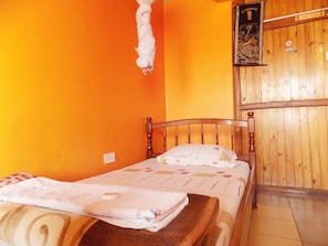Uma cama de solteiro com cabeceira de madeira, um travesseiro branco e uma toalha dobrada sobre a estrutura de madeira.