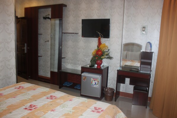 A hotel room with a bed, a desk, a small refrigerator, a TV, a shower, and slippers by the door. - Song Anh hotel (Ho Chi Minh City)