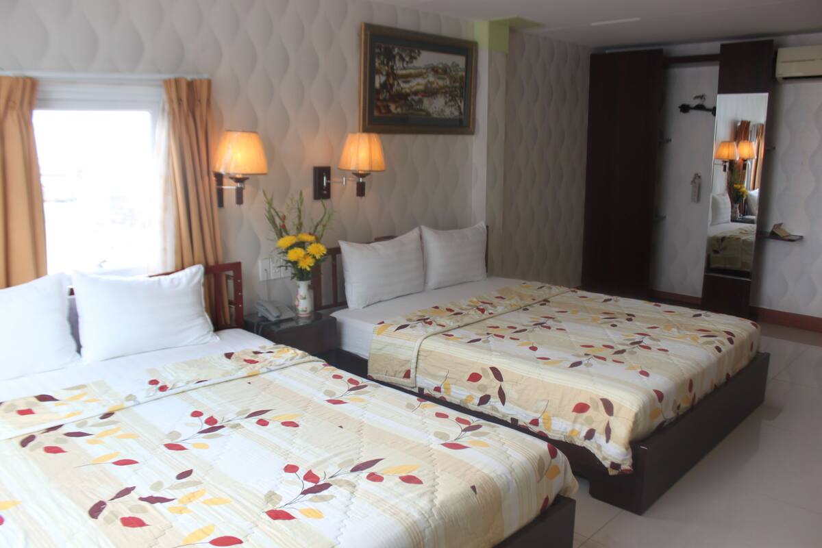 Ein Hotelzimmer mit zwei Betten, einem Nachttisch mit Lampen, einer Blumenvase und einem Bild an der Wand.