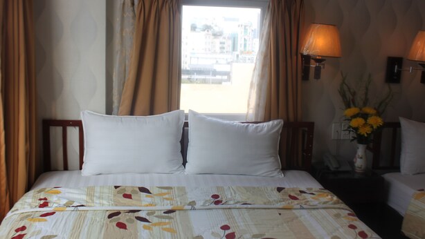 A hotel room with a bed, a nightstand with a lamp, and a window with curtains.