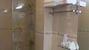 A bathroom with a glass-enclosed shower, a toilet, a sink with a marble countertop, and a towel rack with folded towels.