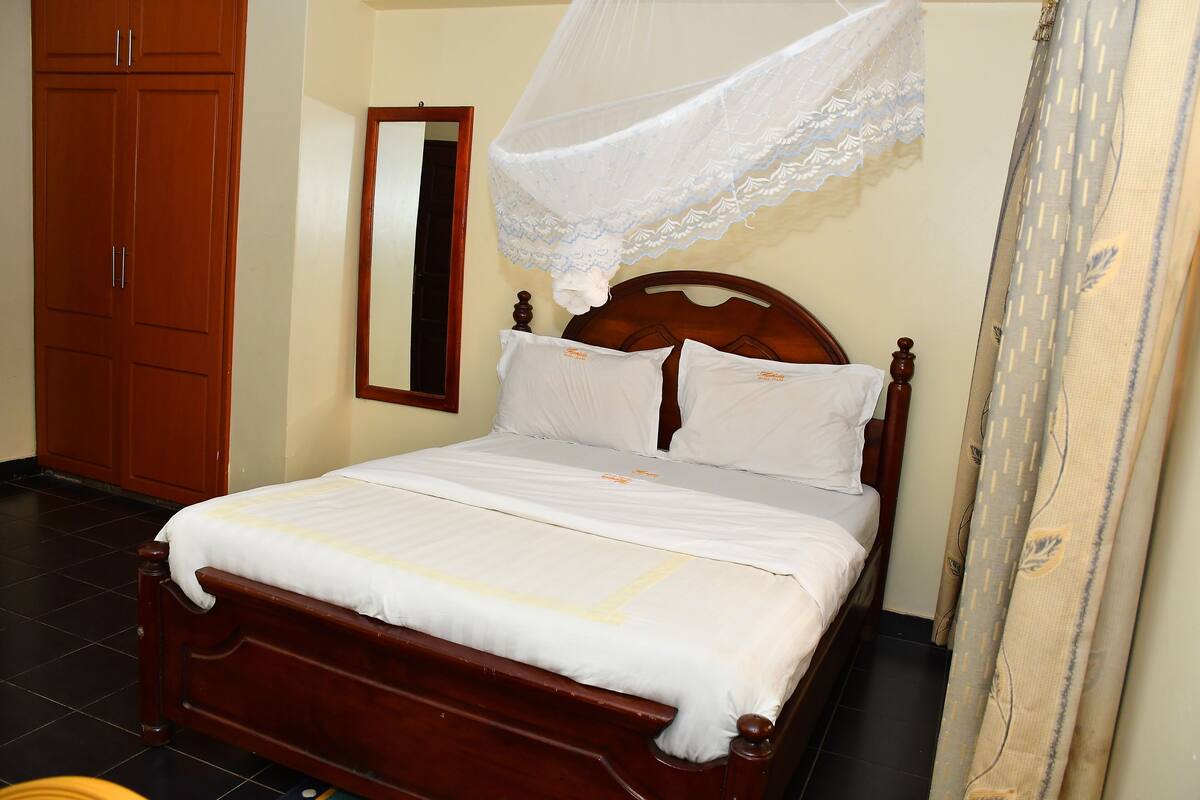 A neatly made bed with a wooden headboard, a white canopy, and a mirror on the wall.