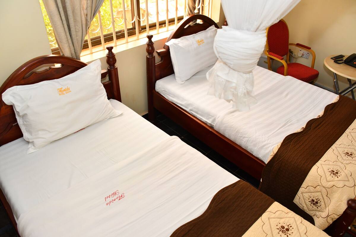 Two wooden beds with white linens and pillows, a red chair, a small round table, and a window with curtains.