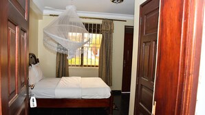 A bedroom with a bed, a hanging light fixture, a window with curtains, and a door. - Florida Hotel (Kampala)