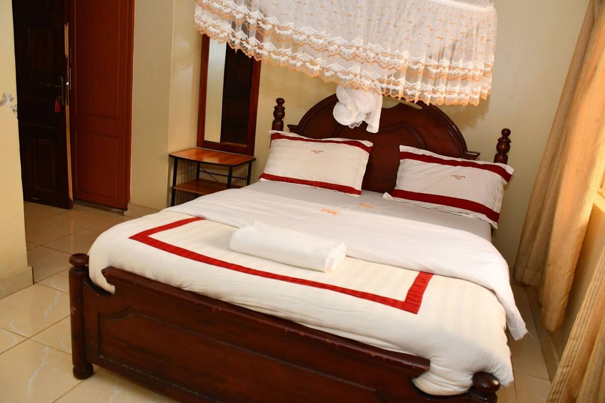 A neatly made bed with white and red bedding, a wooden headboard, and a small bedside table.