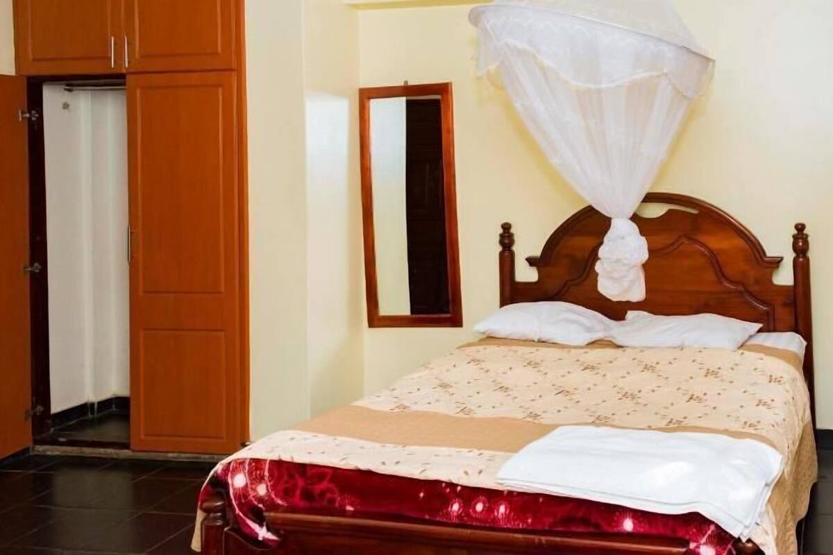A bedroom with a wooden bed, a white canopy, a mirror, and a door.