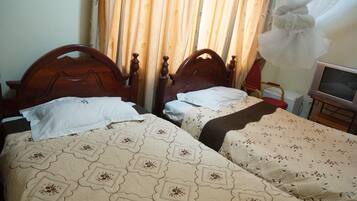 Duas camas de madeira com roupa de cama florida, uma televisão em um suporte e uma cortina com padrão de folhas.