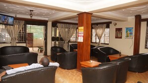 A lobby with leather sofas, a wooden pillar, and a television screen. - Florida Hotel (Kampala)