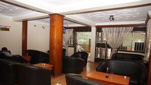 A hotel reception area with leather seating, a reception desk, and a view of the outside through a gate. - Florida Hotel (Kampala)