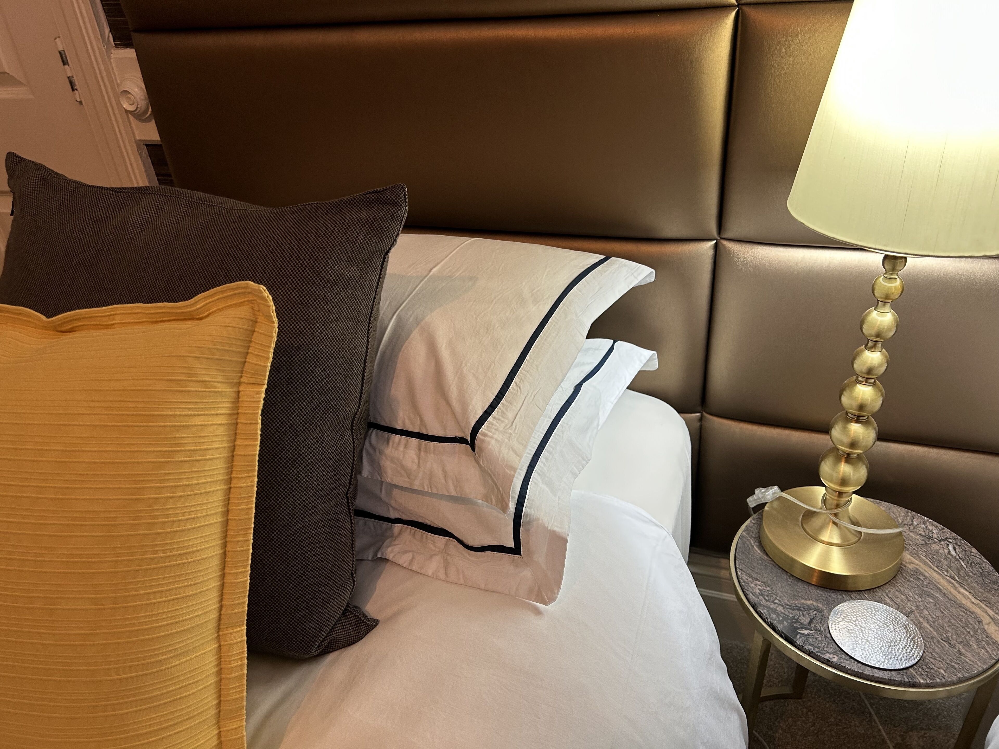 A neatly made bed with multiple pillows and a bedside table with a lamp.