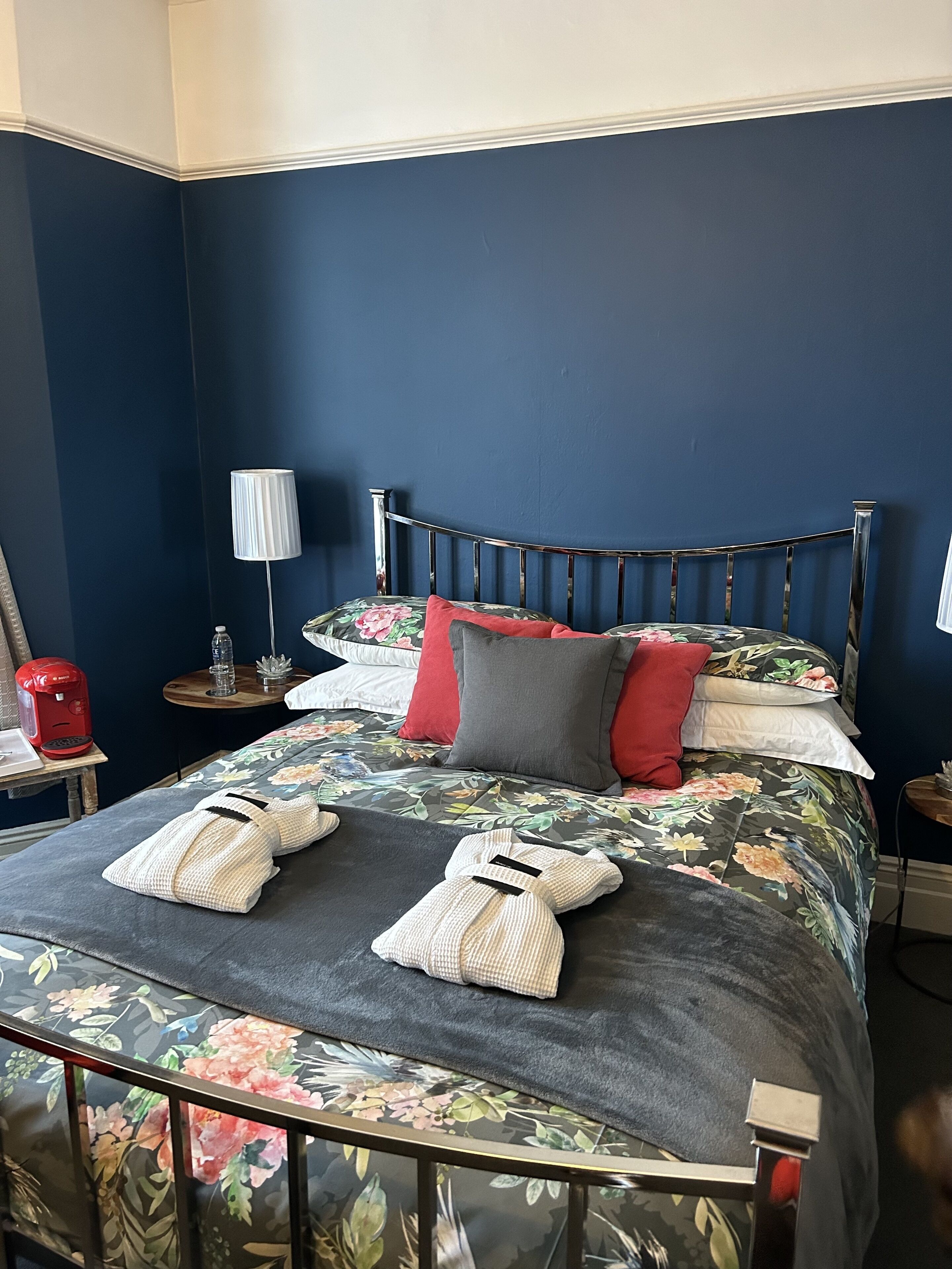 A neatly made bed with floral bedding, two towels, and a red and gray pillow.