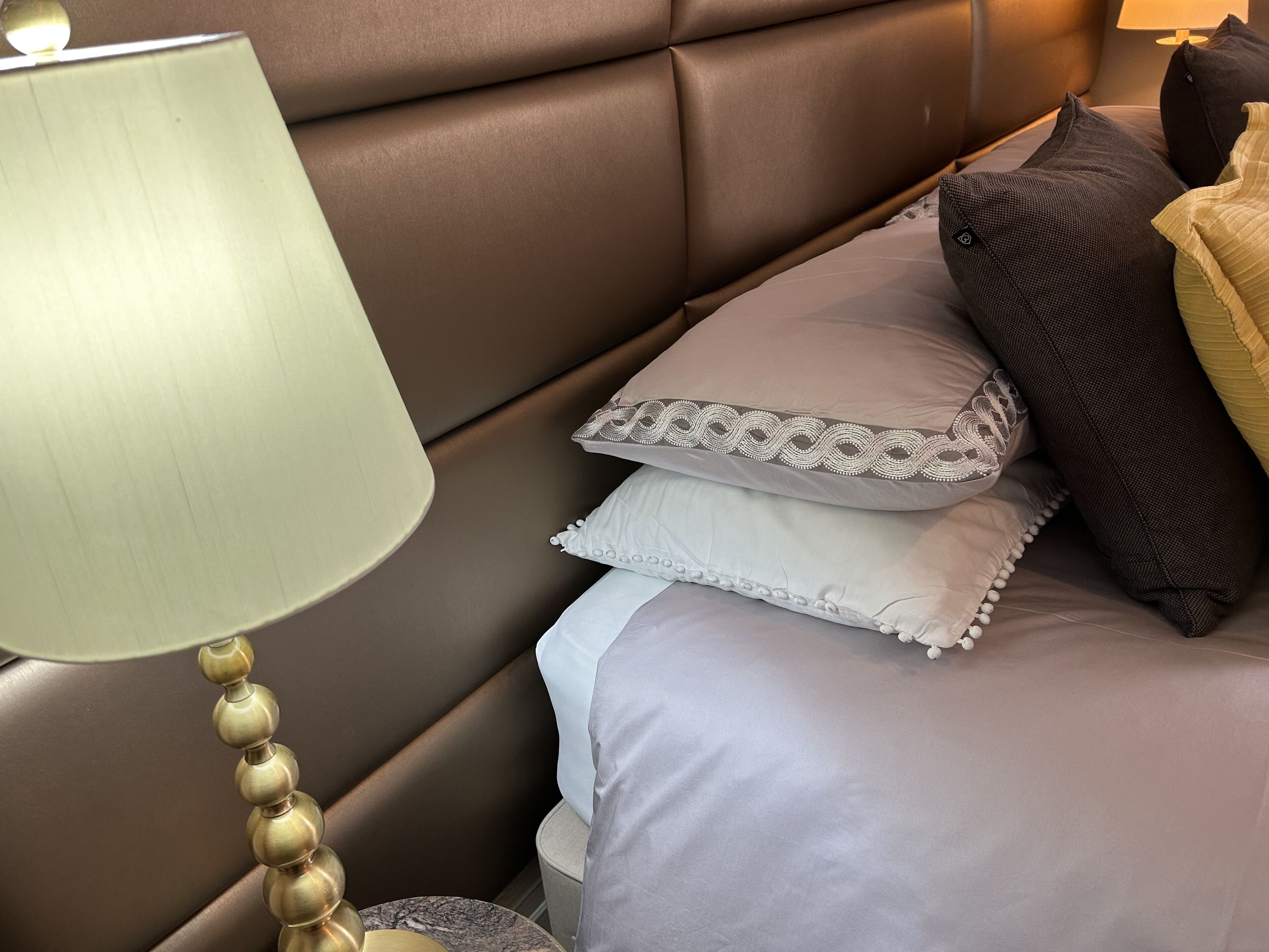 A neatly made bed with a headboard, a bedside lamp, and several pillows.