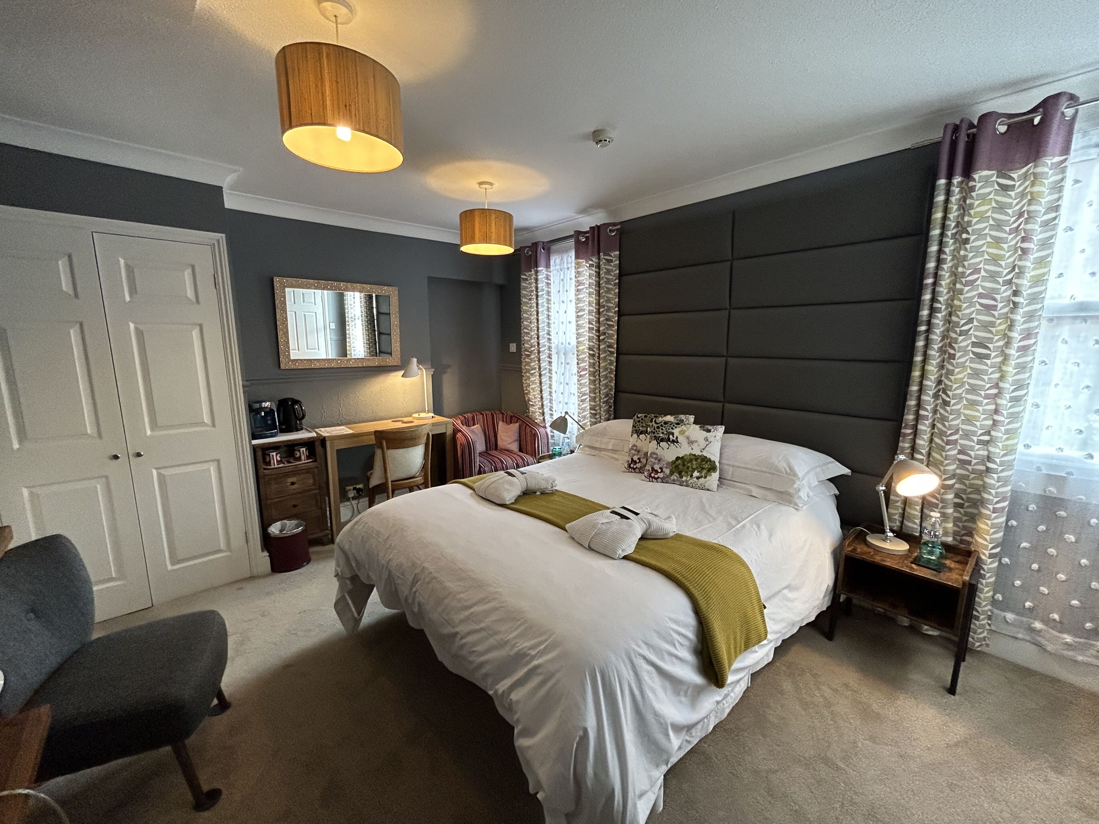 A bedroom with a large bed, bedside tables, a desk, a chair, a wardrobe, and a mirror.
