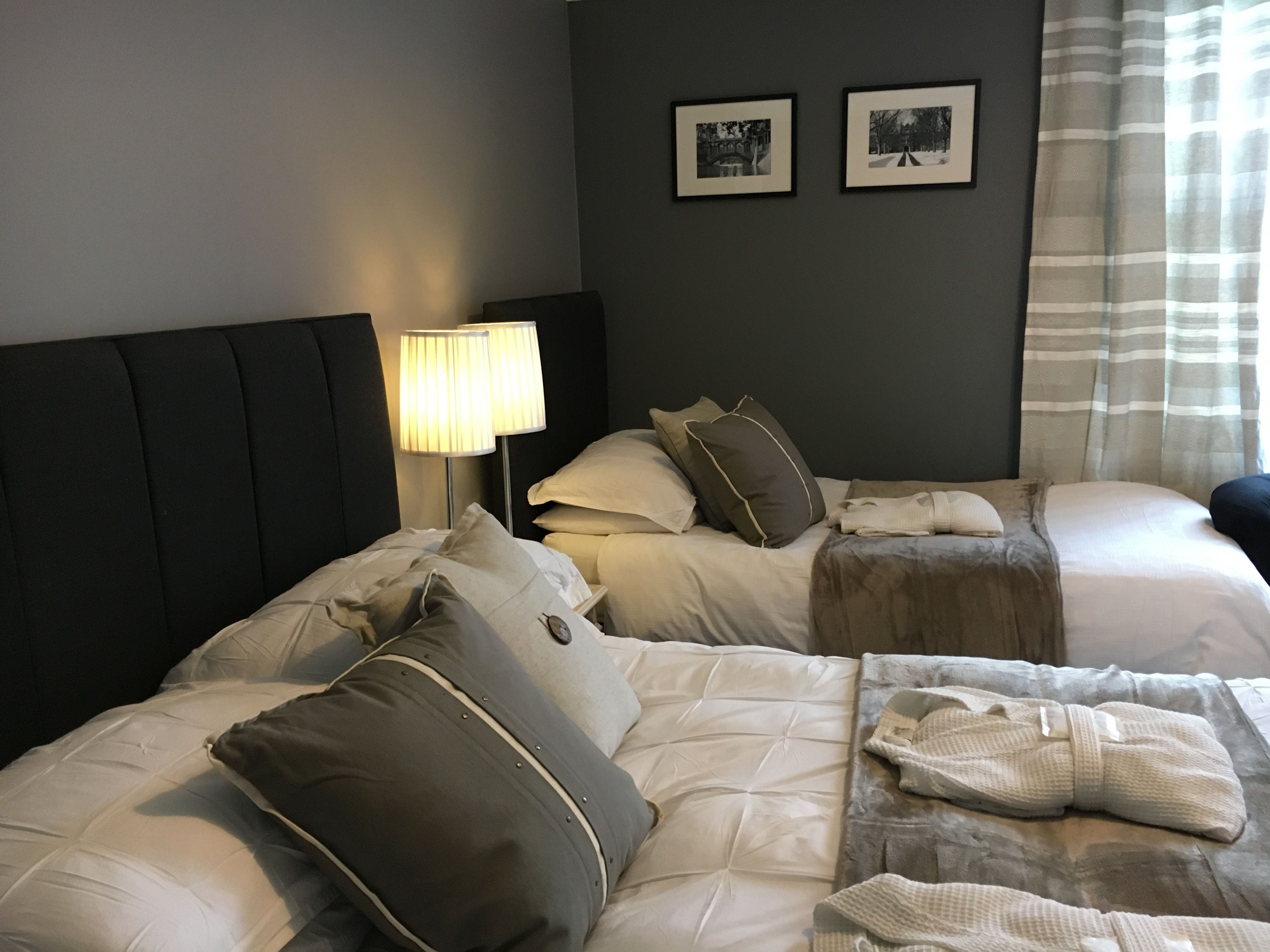 Quarto de hotel com duas camas, uma mesa de cabeceira com abajur e duas fotos emolduradas na parede.