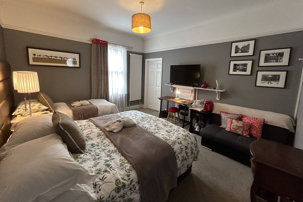 A hotel room with two beds, a TV, a desk with a lamp, and framed pictures on the wall.