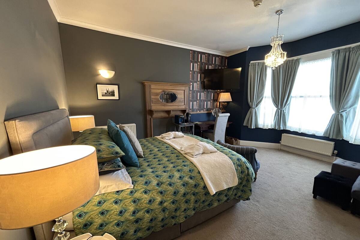 A bedroom with a large bed, a desk, a bookshelf, and a television.