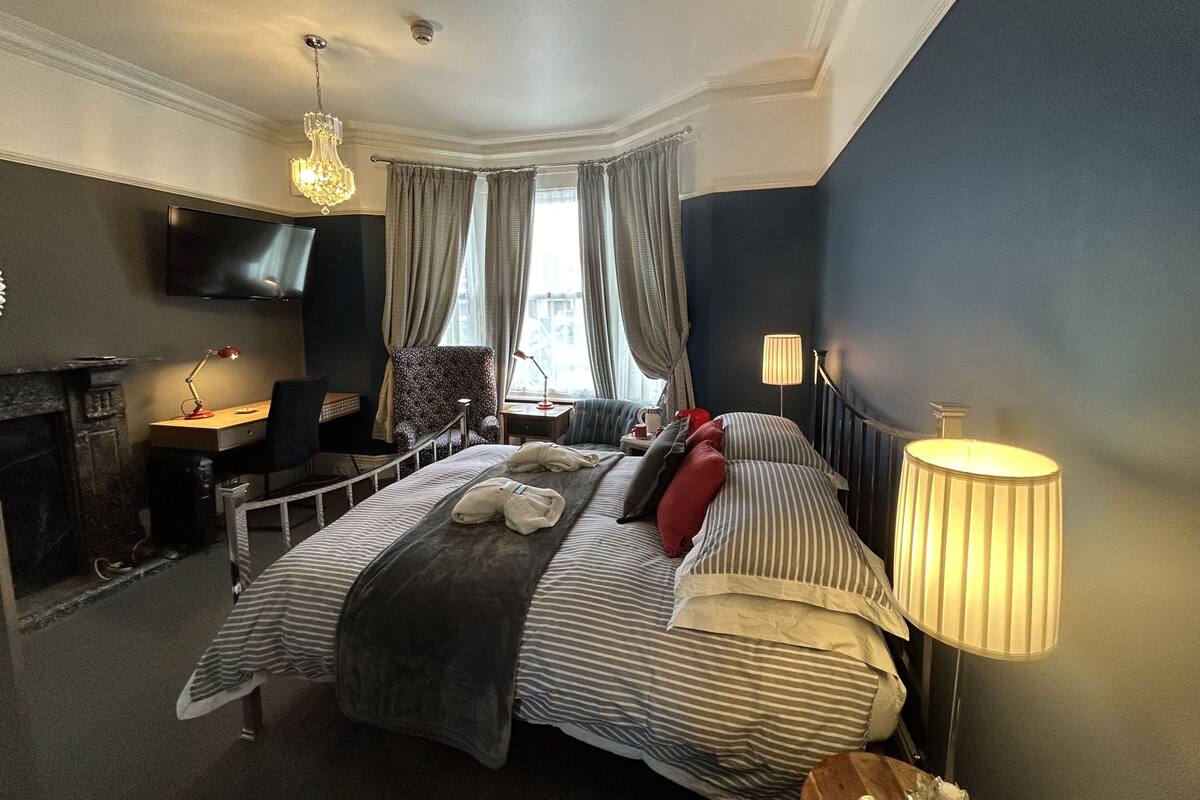 A hotel room with a bed, a desk, a chair, a TV, and a window with curtains.