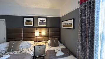 Ein Hotelzimmer mit zwei Betten, einem Nachttisch mit Lampen und gerahmten Bildern an der Wand.
