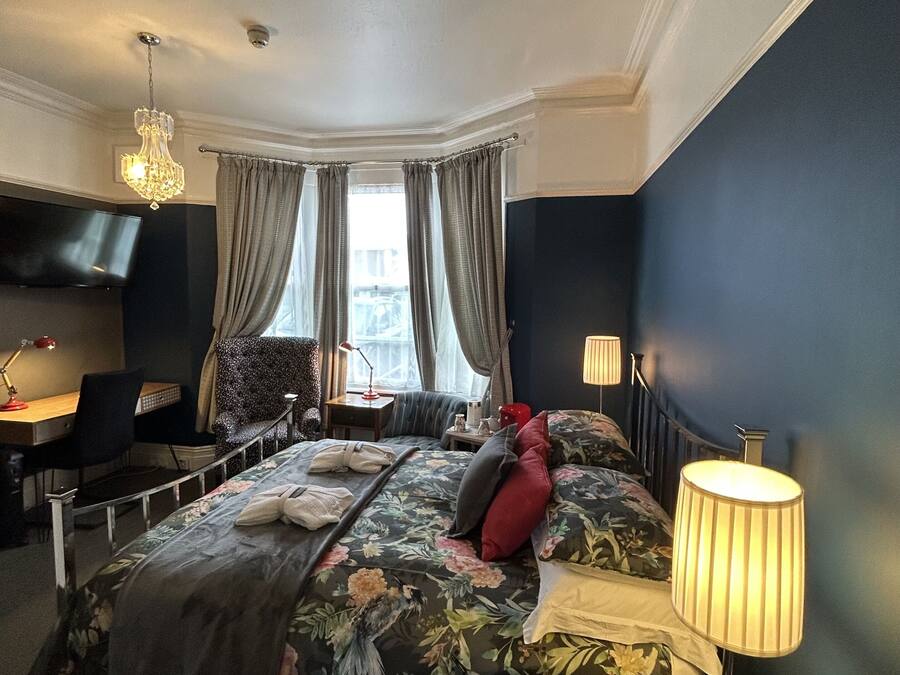 A hotel room with a large bed, a desk, a chair, a TV, and a chandelier.