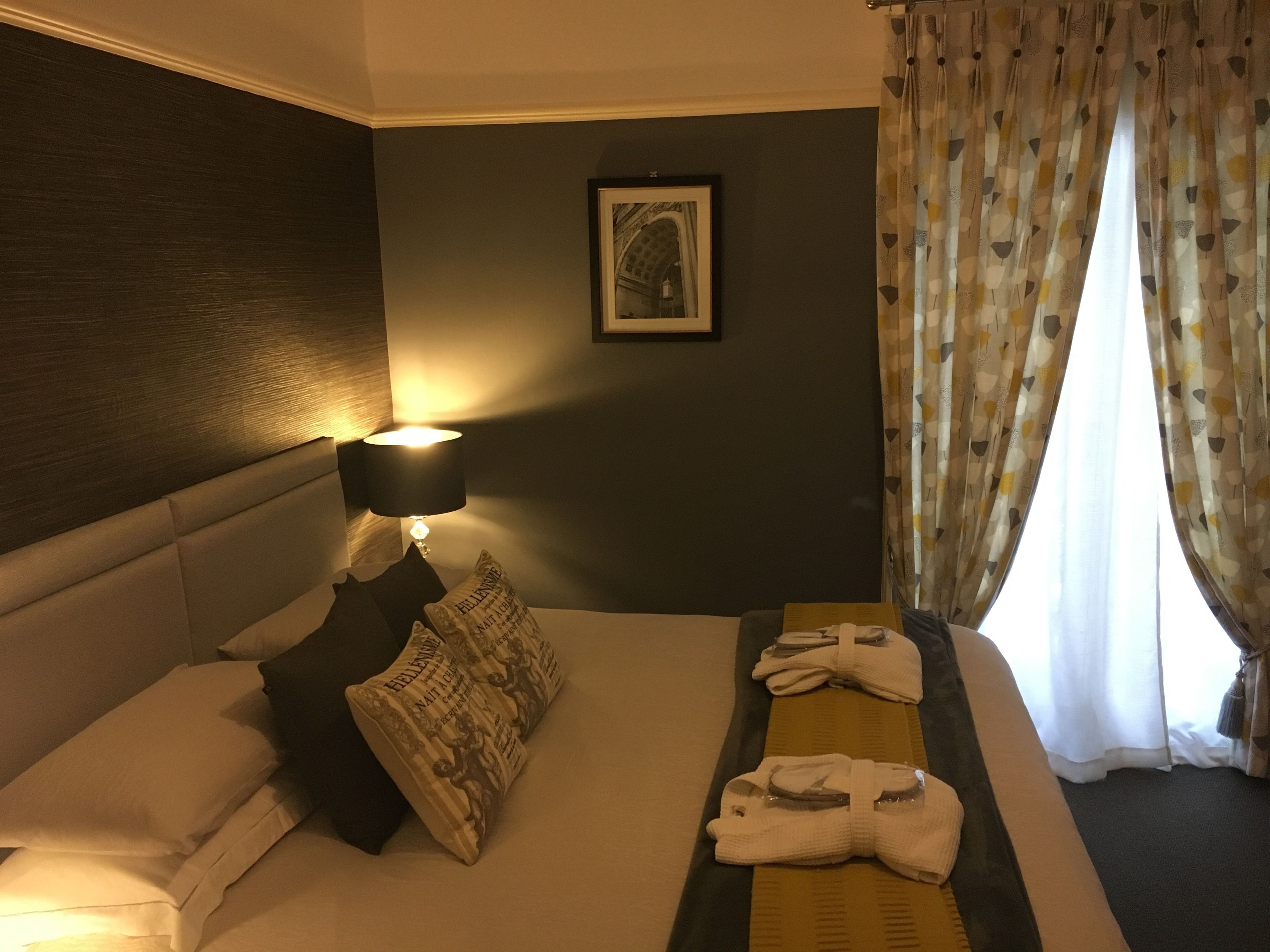 Habitación de hotel con cama, almohadas, un cuadro enmarcado en la pared, lámpara y ventana con cortinas.